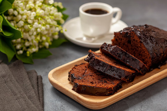 Ciasto czekoladowe na drewnianej tacce, kawa, konwalie i ścierka kuchenna