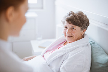 Elderly woman in white bathrobe and young volunteer at nursing home - obrazy, fototapety, plakaty