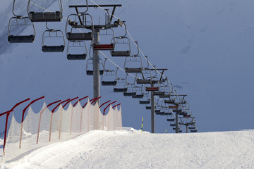 Snowy ski slope and chair-lift on high mountains at sunny winter evening