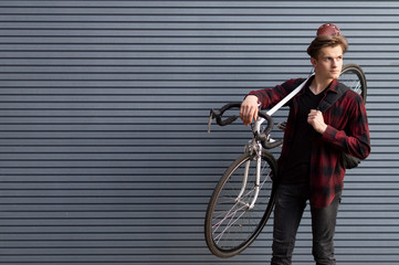 young handsome guy carries a broken bike on his shoulders against the wall, the student goes on foot
