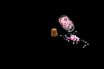 fallen down glass bottle filled with sweet pearls on black background with reflection