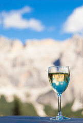 Glass of chilled white wine on a rocky mountain background. Hiking in Dolomites, Italy