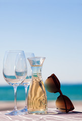 The carafe of white wine and a glass of wine with sunglasses by Garda Lake beach