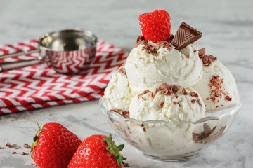 Vanilla ice cream decorated with strawberries and chocolate chips. Delicious frozen dessert. Cooling summer snack. Light photo.