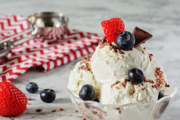 Delicious frozen dessert. Vanilla ice cream decorated with strawberries, blueberries and chocolate chips. Cooling summer snack. Light photo.