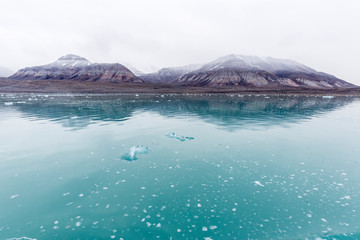 Pieces of glacier ice Nordenskiöldbreen near Pyramiden, snowcaped mountain, on the coast of...