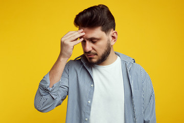 Sad and upset young boy holding head down and thinking about work. Bearded man in casual shirt isolated over orange wall