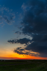 The sky with bright clouds lit by the sun after sunset over the field.