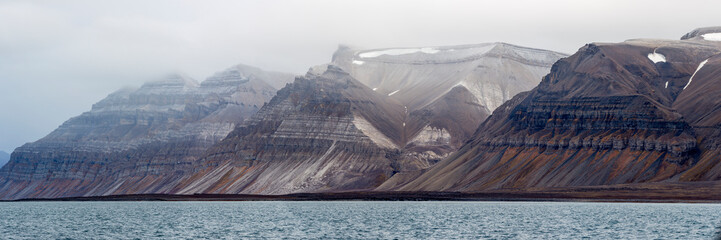 Billon year old jagged rock formations with different green moss and snow within, Svalbard,...