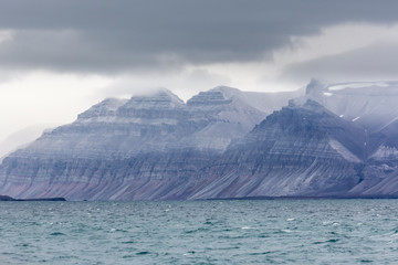 Billon year old jagged rock formations with different green moss and snow within, Svalbard, Isfjorden, Norway