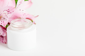 Face cream in white jar on a white background with pink flowers. Concept natural cosmetics, organic beauty, flower arrangement. Copy space.
