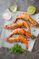 Grilled giant tiger prawns on paper with lemon and spices on vintage dark background, top view, copy space. Seafood dinner.