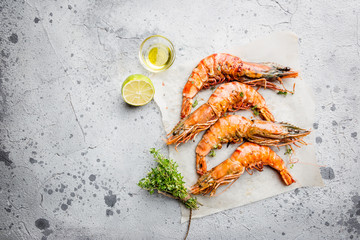 Grilled giant tiger prawns on paper with lemon and spices on light gray background, top view, copy space. Seafood dinner.