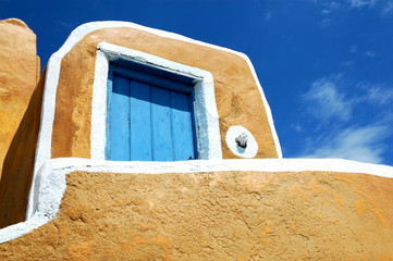 Yellow building with blue door in Oia, Santorini, Greece with a background of blue sky and clouds