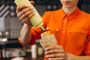 Vinnitsa, Ukraine 10.05.2019: Workflow in Fast Food Cafe: The girl is preparing a French hot dog with ketchup and mustard and sells it to the buyer