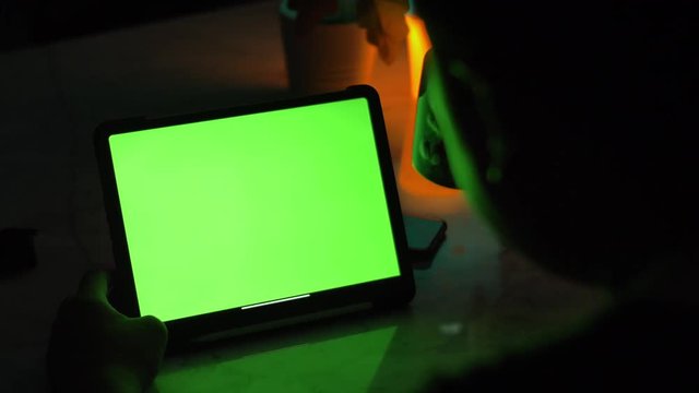 Over the shoulder view of asian man using tablet computer . Green screen of technology being used. Chroma Key tablet.