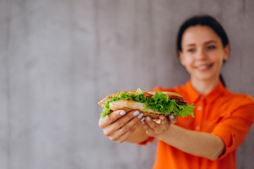 a pretty girl holds a delicious sandwich with vegetables and meat and salad. An ideal concept for advertising a cafe, restaurant, or fast food with sandwiches