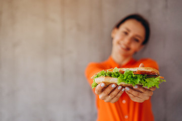 Fototapeta a pretty girl holds a delicious sandwich with vegetables and meat and salad. An ideal concept for advertising a cafe, restaurant, or fast food with sandwiches obraz