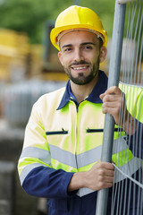 portrait of construction worker stood by metal fence