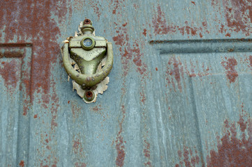 The paint has long ago peeled away and the door knocker on this exterior door shows the signs of rust and grunge.