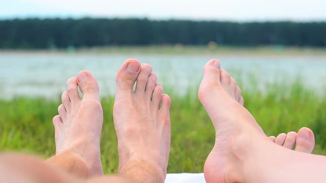 Close up of young couple feet relaxing on beach. Woman. Man. Lake. Landscape. Legs. Blur Background