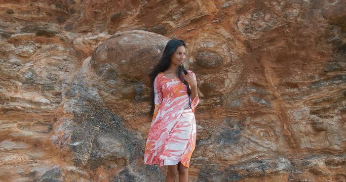 Portrait of a beautiful young South Asian girl standing near a red sandy-clay natural wall. in slow motion. Shot on Canon 1DX mark2 4K camera