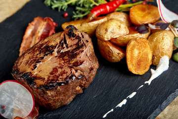 Beef steak served with baked potatoes and vegetables,black background, close-up. concept food.