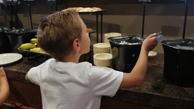 Boy Dishes Up Cottage Cheese In Breakfast Buffet. A young boy in a hot breakfast buffet line serves himself some cottage cheese and then walk to the table.