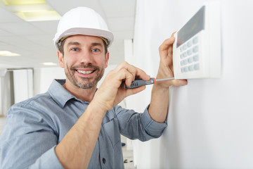 happy male plumber fixing thermostat at home