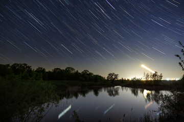 Trail of stars in the night sky around the North Star over the lake. photographed with a long exposure on the background.