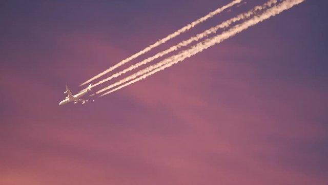Jet aircraft leaving vapor contrails on a pastel pink sky. Tracking