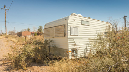 Retro abandoned travel trailer RV in an overgrown yard