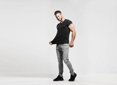 Muscular model sports young man in grey jeans and black t-shirt on a grey background. Fashion portrait of brutal sporty sexy strong muscle guy with a modern trendy hairstyle. Model, fashion concept.