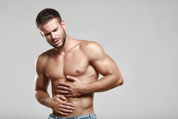 Young man suffering from stomach ache. Causes of abdominal pain include gastritis, stomach ulcer, food poisoning, diarrhea or IBS. Gray background. Healthcare, medical and sickness concept.