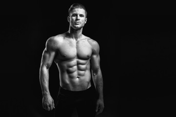 Fototapeta na wymiar Muscular model young man on dark background. Black and white fashion portrait of strong brutal guy with modern trendy hairstyle. Sexy naked torso six pack abs. Male flexing his muscles. Sport concept.