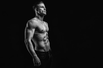 Muscular model young man on dark background. Black and white fashion portrait of strong brutal guy with modern trendy hairstyle. Sexy naked torso six pack abs. Male flexing his muscles. Sport concept.