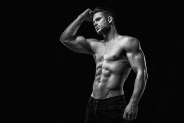 Fototapeta na wymiar Muscular model young man on dark background. Black and white fashion portrait of strong brutal guy with modern trendy hairstyle. Sexy naked torso six pack abs. Male flexing his muscles. Sport concept.