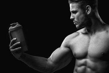 Model sports young man on dark background. Black and white portrait of muscle guy with protein...