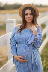 Beautiful portrait of cheerful pregnant woman in blue dress and knitted hat. Lady smile