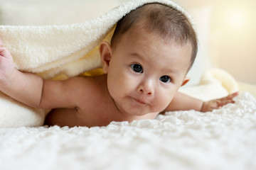 Cheerful cute baby looking at camera under white blanket. Innocence baby crawling on white bed with towel on his head at home.