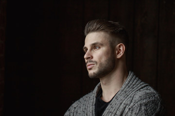 Muscular model young man with beard in knitted sweater on dark background. Fashion portrait of brutal sporty sexy strong muscle guy with modern trendy hairstyle. Model, fashion concept.