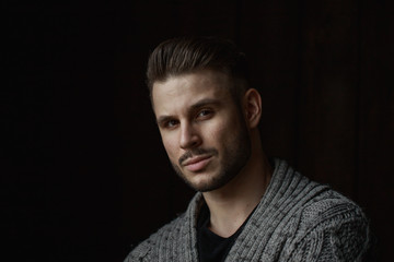 Muscular model young man with beard in knitted sweater on dark background. Fashion portrait of brutal sporty sexy strong muscle guy with modern trendy hairstyle. Model, fashion concept.