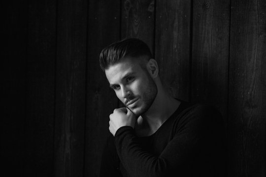 Black and white. Muscular model young man with beard in black t-shirt on dark wooden background. Fashion portrait of brutal sporty sexy strong guy with modern trendy hairstyle. Model, fashion concept.