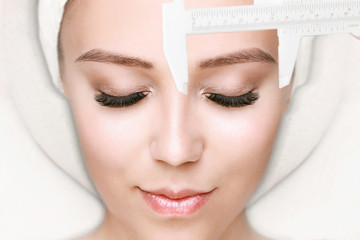 Beautiful young girl with long eyelashes tweezing her eyebrows in a beauty salon. Woman doing eyebrow permanent makeup correction. Microblading brow.