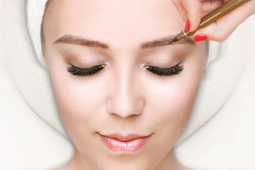 Beautiful young girl with long eyelashes tweezing her eyebrows in a beauty salon. Woman doing eyebrow permanent makeup correction. Microblading brow.