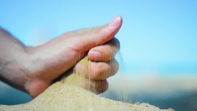 Hand closeup of releasing sand. The sand flows through the hands against a blue ocean. Summer beach vacation. Blur Background. Woman. Tan