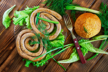 Grilled sausages, corn bun and fork lie on a wooden surface with greens: lettuce, dill, onion and parsley. Picnic - barbecue