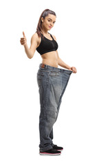 Slim young woman wearing pair of big size jeans showing thumbs up