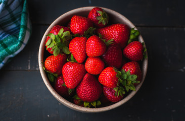 Close-up of fresh strawberries in a bowl on wooden background, top view