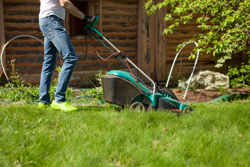 Young man mowing the lawn. Worker doing his job in backyard. Spending summer day in garden. Lawnmower standing on the background of private garden.